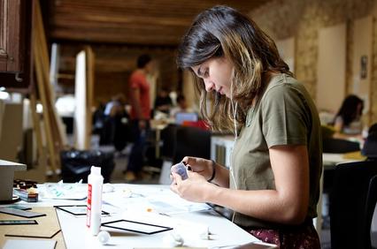 A young woman is focused on crafting at a well-lit workspace.