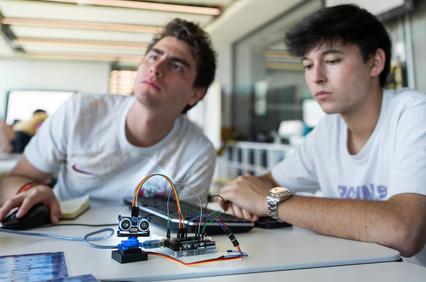 Two young men are working on a technology project with an electronic device on a table.
