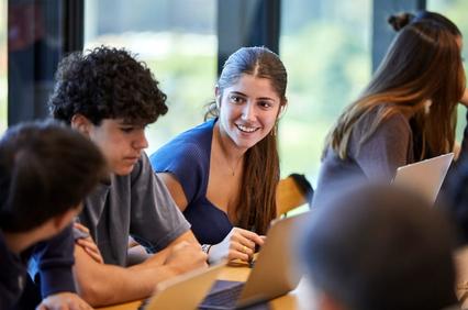 A group of young people engaged in a discussion at a table, with one person smiling.