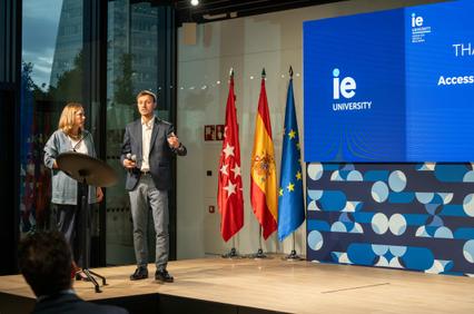 A presentation at IE University with speakers discussing a topic in front of national flags.