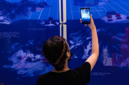 A person is taking a photo of a digital artwork displayed on a wall.