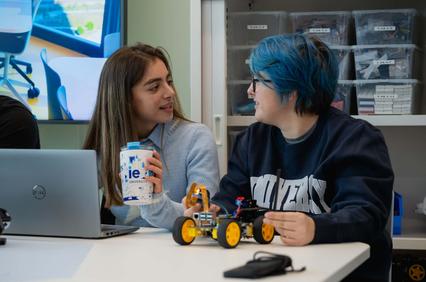 Two young people engaged in conversation while working on robotics projects at a table.