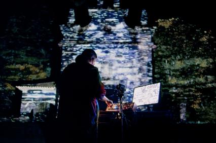 A performer creates music in front of a digitally projected backdrop.