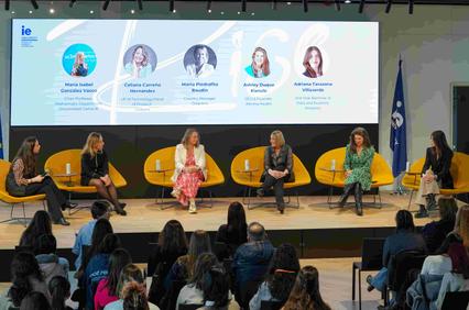 A panel of women discussing various topics in front of an audience at an event.