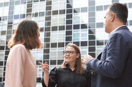 A group of three professionals are engaged in a conversation outdoors near a modern building.