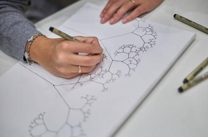 A person is drawing intricate fractal patterns on a sheet of paper.