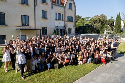 A large group of people joyfully posing outdoors in front of a building.
