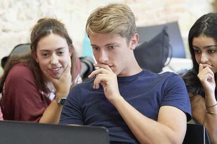 Four young adults are attentively looking at a laptop screen together in a casual setting.