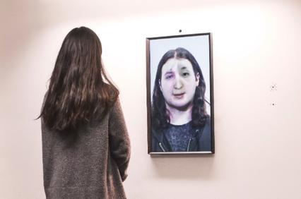 A woman stands in front of a framed digital portrait displayed on a wall.