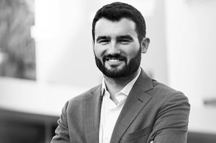 A man in a suit smiling with his arms crossed.