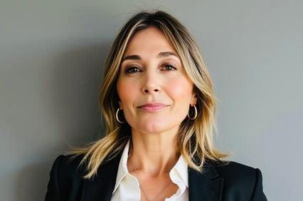 A professional woman wearing a black blazer and white shirt, smiling against a neutral background.
