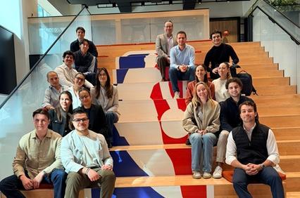 A diverse group of people is seated on steps decorated with an NBA logo.