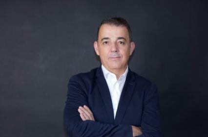 A professional portrait of a middle-aged man standing with arms crossed against a dark background.