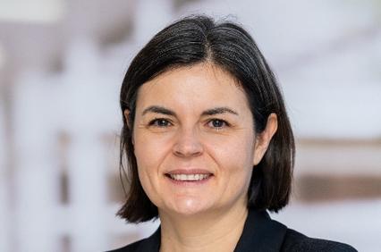 A professional portrait of a smiling woman with short, dark hair, wearing a black blazer over a white top.