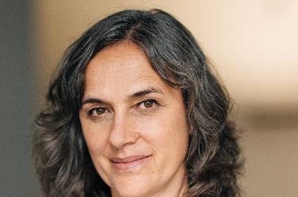 A woman with wavy hair wearing a blue sweater, smiling gently at the camera.