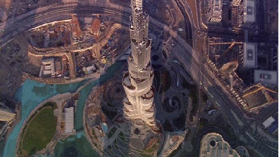 An aerial view of a tall skyscraper surrounded by modern architecture and green spaces.