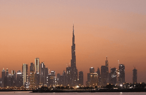 A skyline view of a city at sunset featuring tall buildings and a prominent tower.