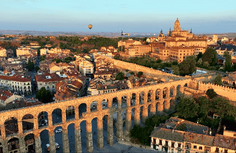A breathtaking aerial view of an ancient aqueduct surrounded by a cityscape and a hot air balloon in the distance.
