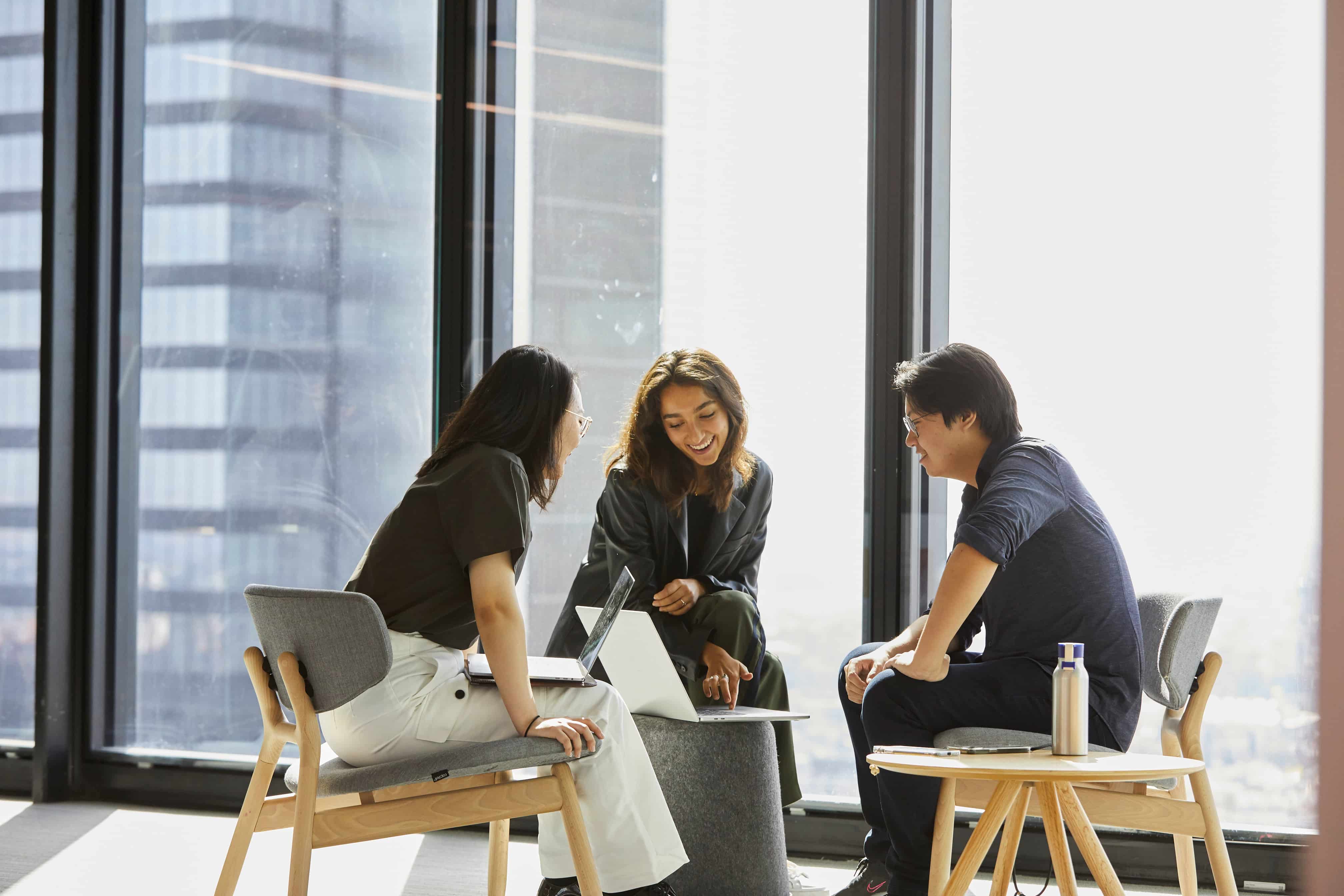 A group of three people collaborating around a laptop in a bright, modern office space.