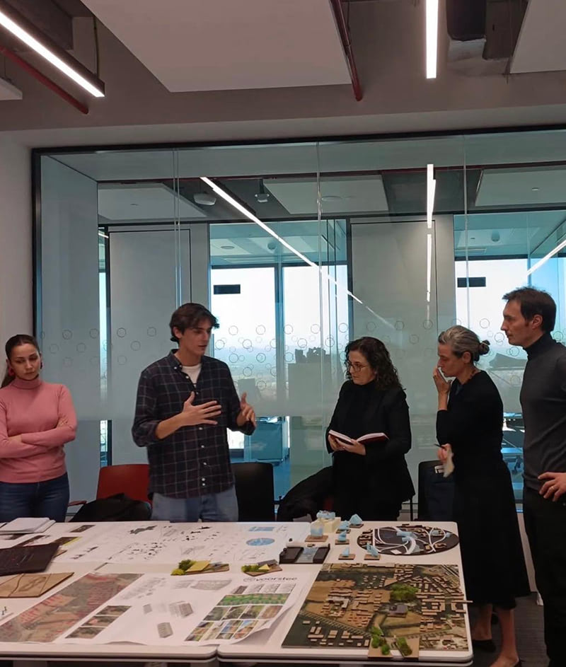 A group of people discussing a project around a table with diagrams and materials.