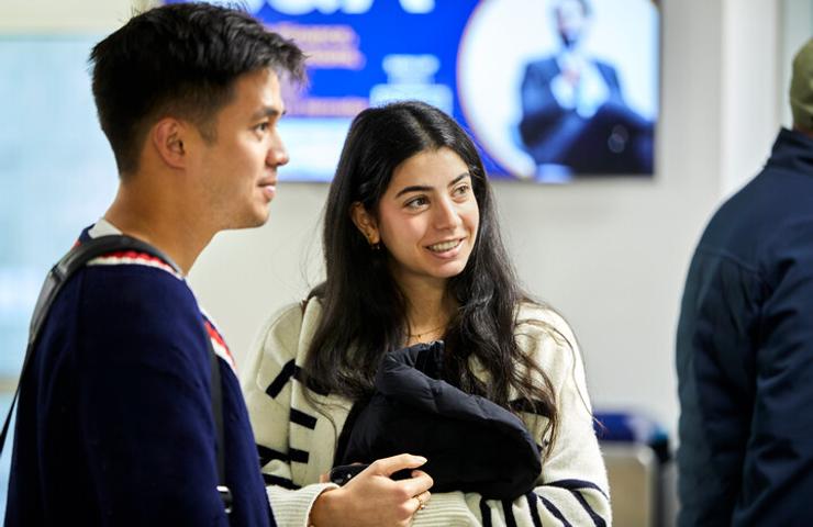 A young man and woman smiling and standing in a public indoor area.