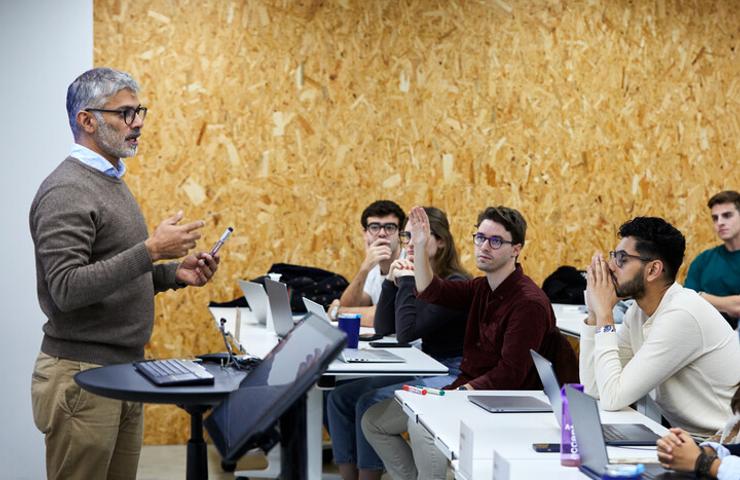 A mature male professor teaching a group of young adult students in a modern classroom.