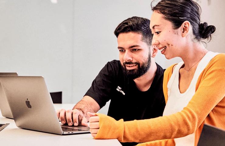 A man and a woman collaborating at a laptop in an office setting.