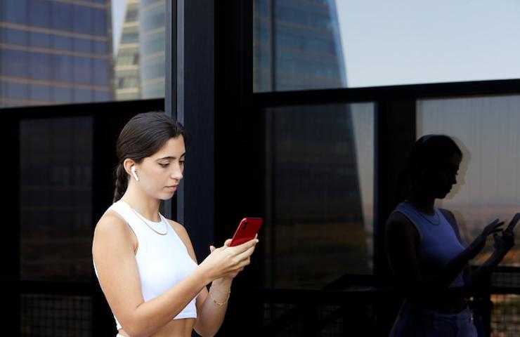 A young woman using her smartphone outdoors in a city setting with reflective windows.