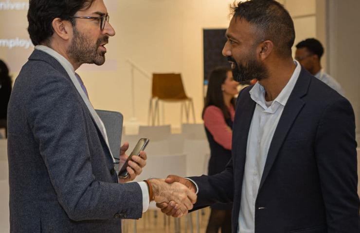 Two men shaking hands and engaging in conversation in a modern office setting.