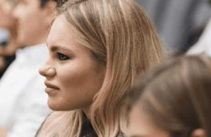 A young woman is sitting and listening attentively in a conference or seminar setting with other attendees in the background.