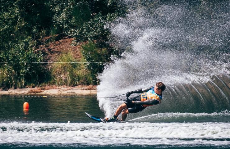 A person waterskiing on a lake, creating a large spray of water.