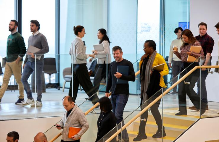 A group of diverse people walking in different directions inside a modern office building.