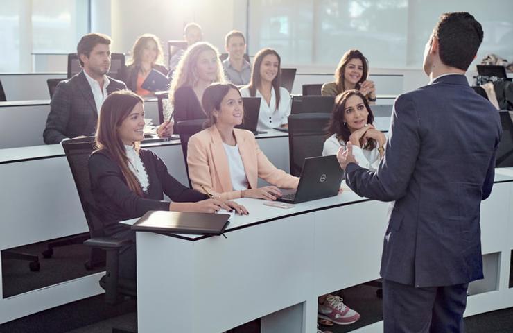 A professional in a suit is presenting to a group of attentive colleagues in a modern office setting.