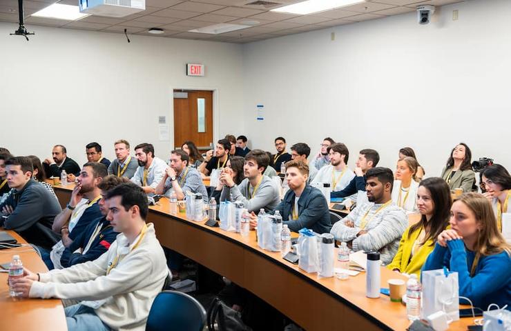 A group of young adults sitting in a classroom setting, actively listening to a speaker out of view.