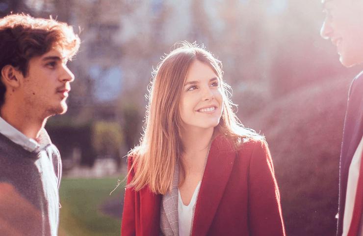 Three young adults chatting and smiling in a sunlit outdoor setting.