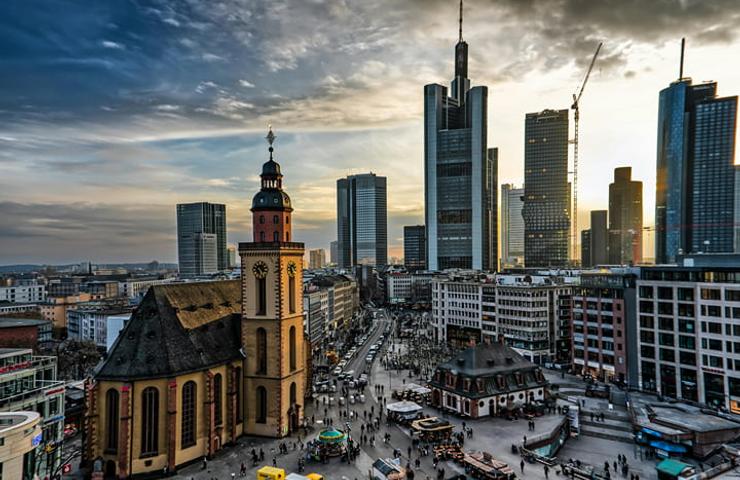 A cityscape shot capturing an old church contrasted against modern skyscrapers under a dramatic sky at sunset.