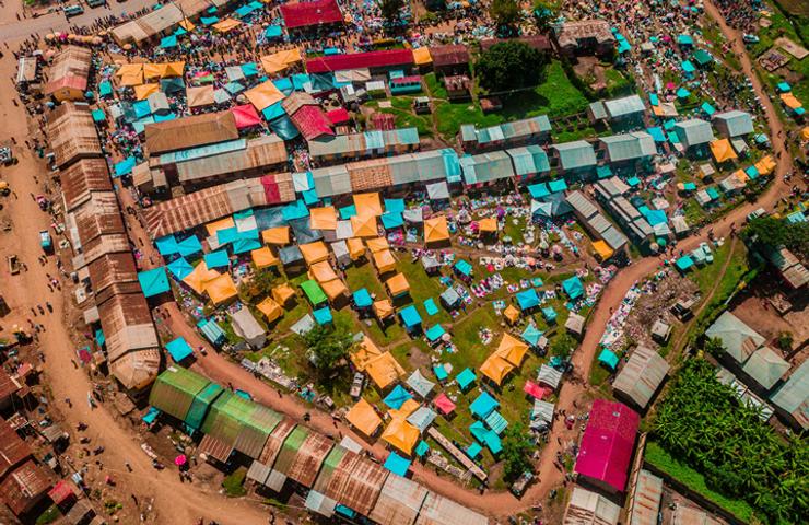 Aerial view of a colorful market set up in a densely packed village with varied roof colors.