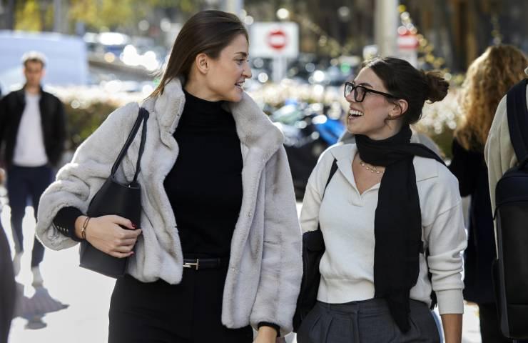 Two women walking and laughing together on a sunny city street