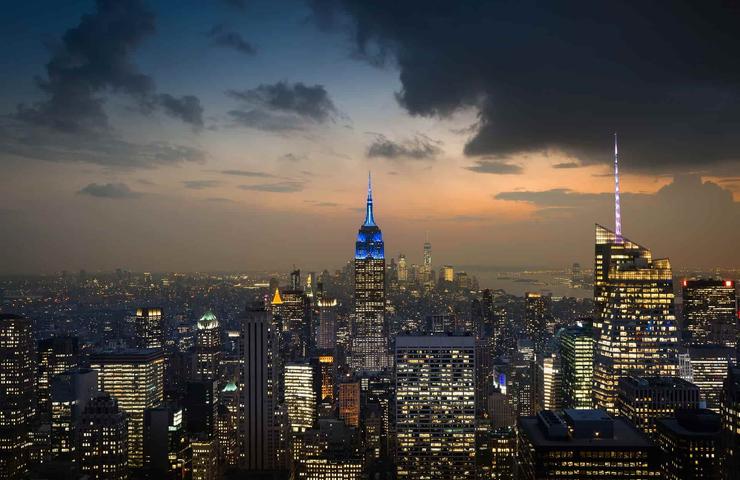 A panoramic view of a city skyline at dusk, featuring prominent skyscrapers illuminated against a twilight sky.