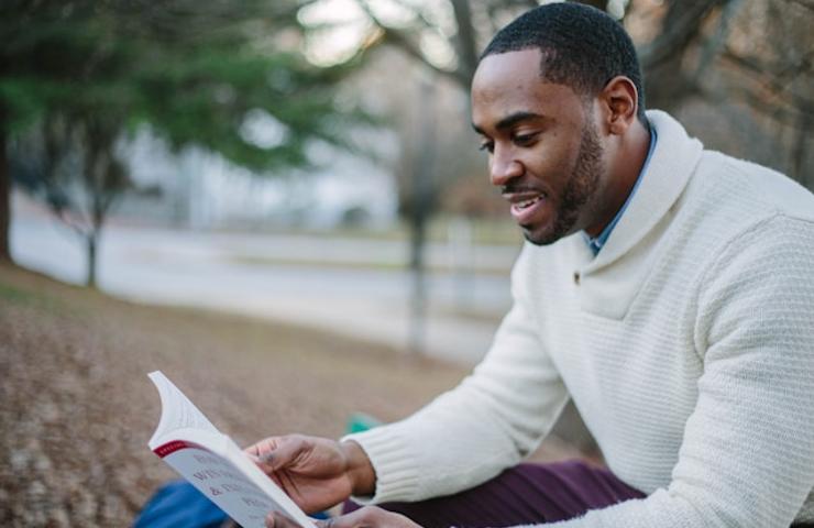 A man reading a book in an outdoor setting.