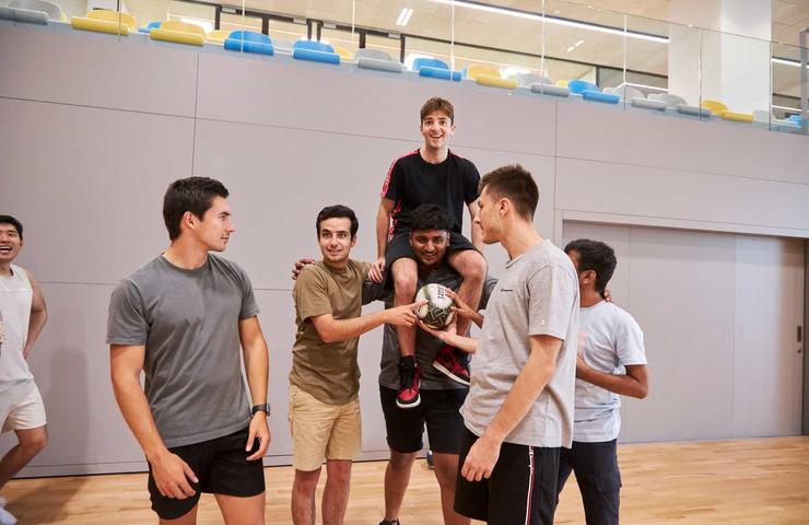 A group of young men engaging in a casual game of indoor soccer, celebrating together in a sports hall.