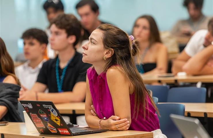 A young woman is attentively listening during a lecture in a classroom filled with students.