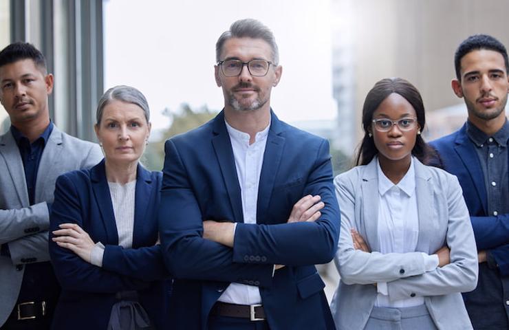 A group of five diverse professional individuals standing confidently in business attire.