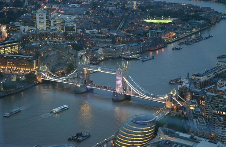 Aerial view of Tower Bridge in London during twilight, featuring city lights and the Thames River.