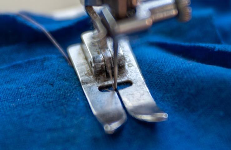 A close-up view of a sewing machine foot pressing against a piece of blue fabric.