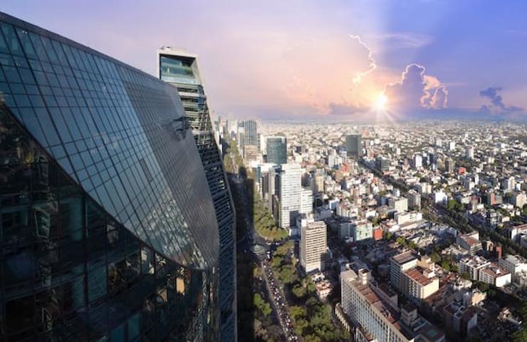 An aerial view of a modern cityscape with a prominent glass building and a sunrise in the background.