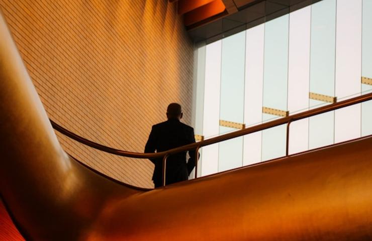 A silhouette of a man standing on a balcony with modern architecture in the background.