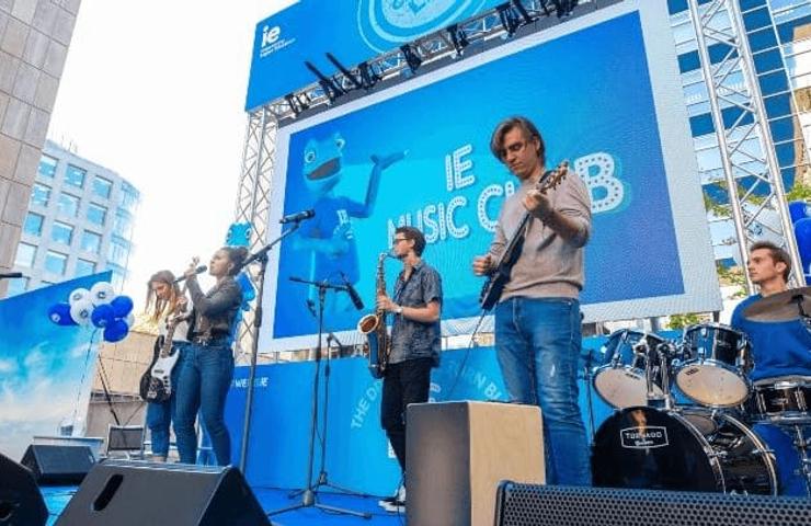 A band performs on stage at an outdoor music event with a blue-themed backdrop.