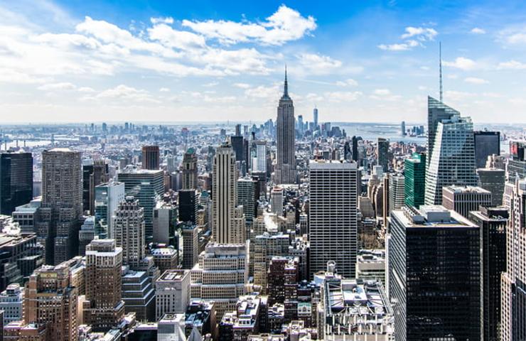 A sprawling urban skyline featuring the Empire State Building under a clear blue sky.