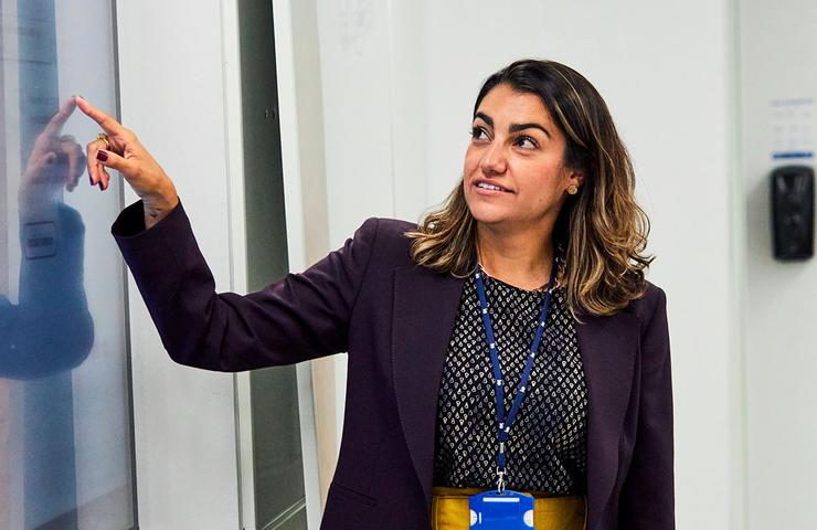 A woman in professional attire is presenting or explaining something on a whiteboard.